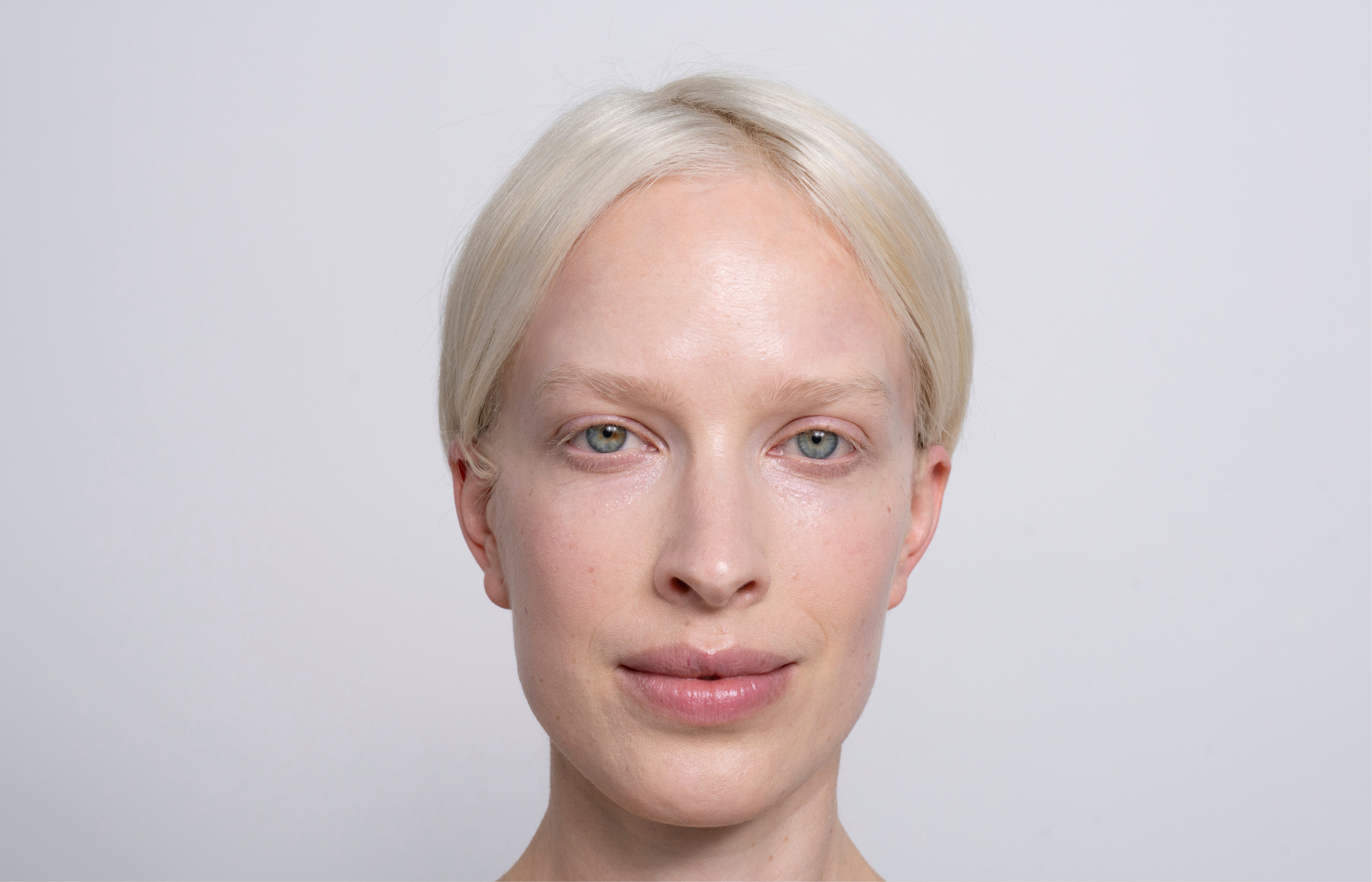 Een vrouw met wit haar, blauwe ogen en een gladde huid kijkt alert en aandachtig in de camera.
