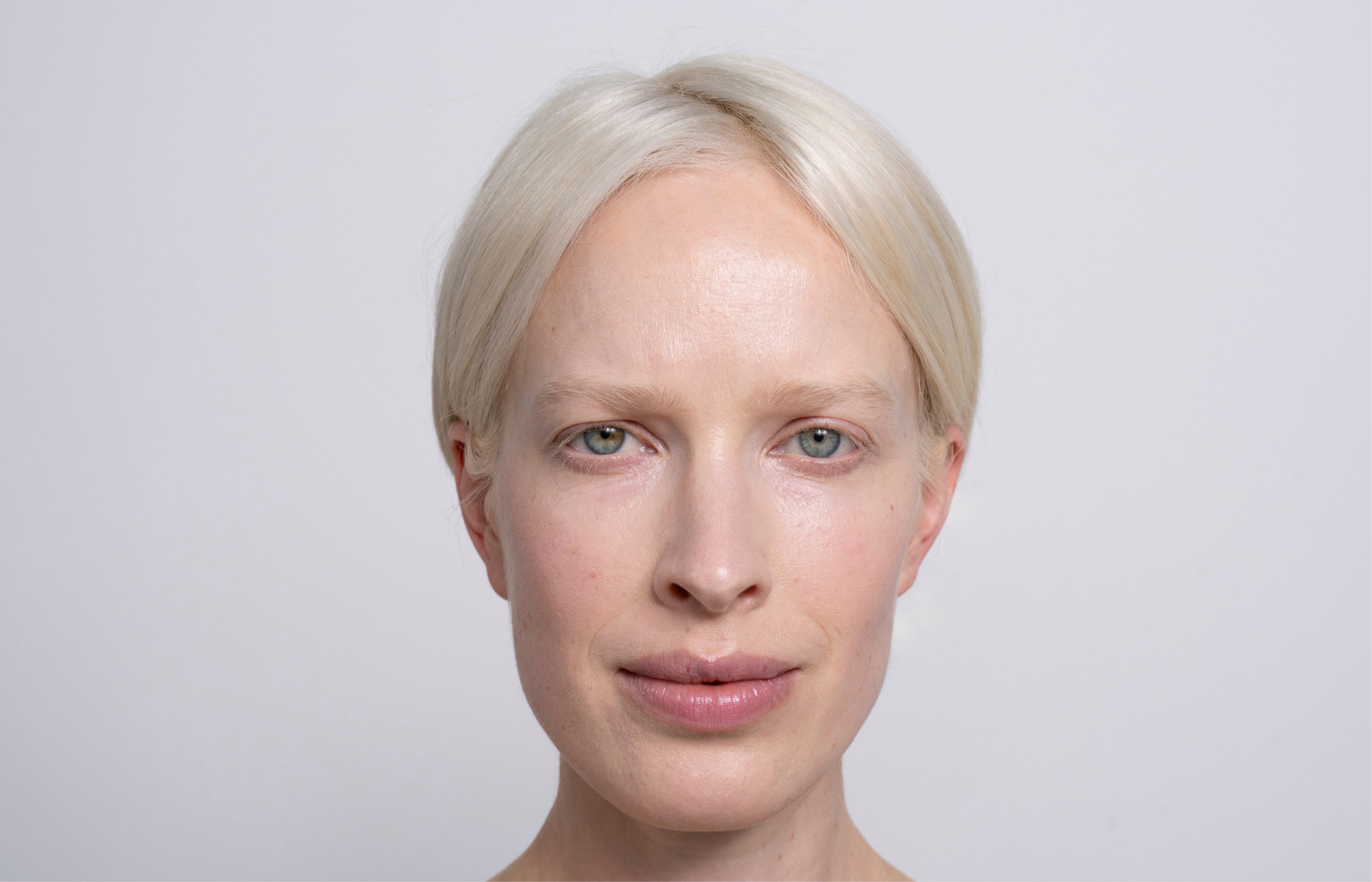 Een vrouw met wit haar en blauwe ogen kijkt vermoeid in de camera.