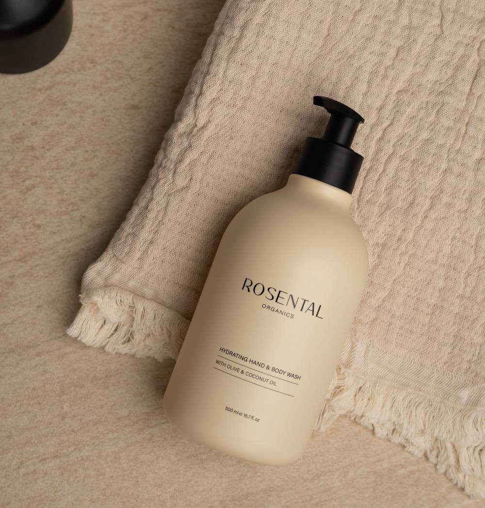 Hydraterende hand- en lichaamszeep in een beige pompdispenser, liggend op een beige handdoek op een marmeren oppervlak.