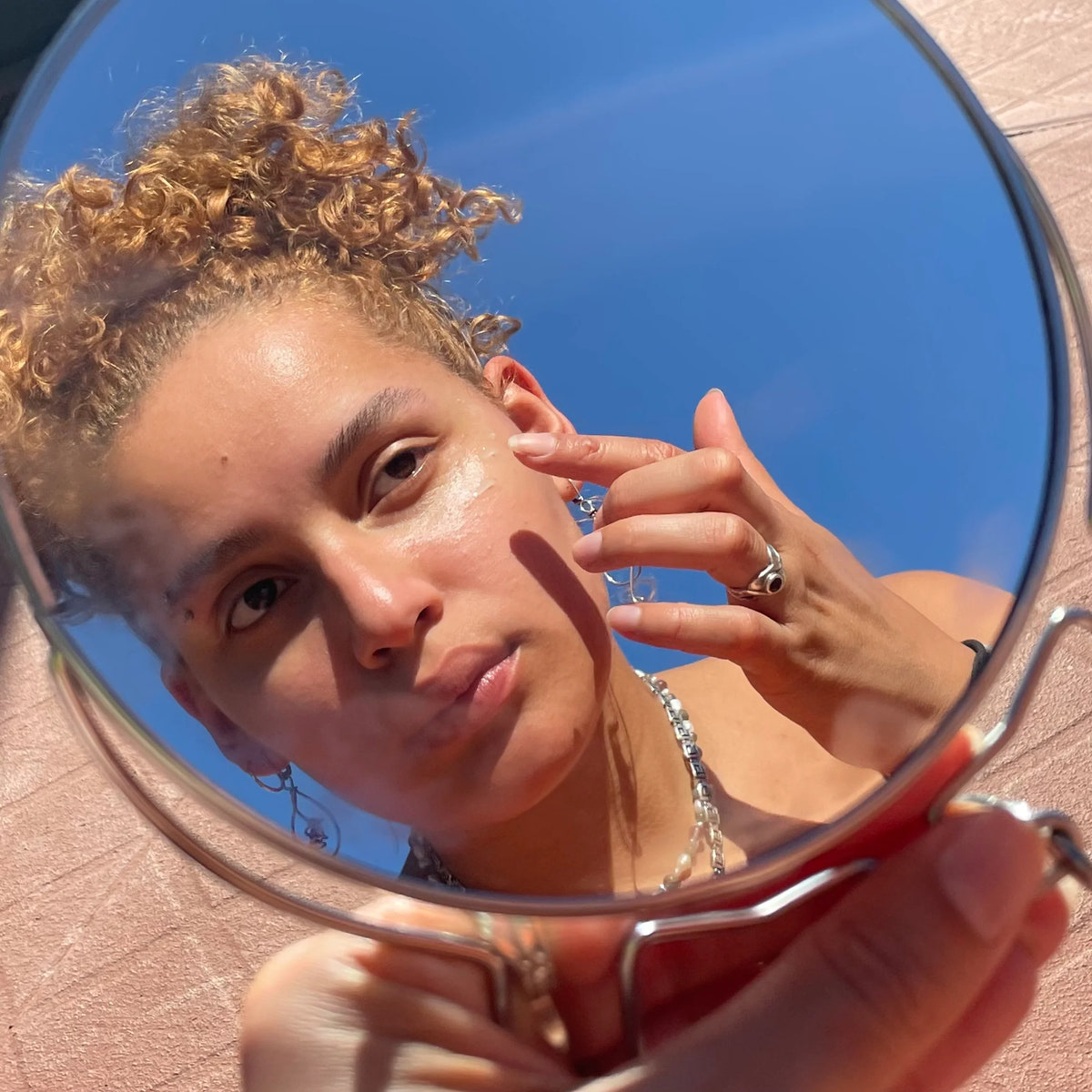De weerspiegeling van een vrouw die een product van Rosental Organics op haar gezicht aanbrengt.