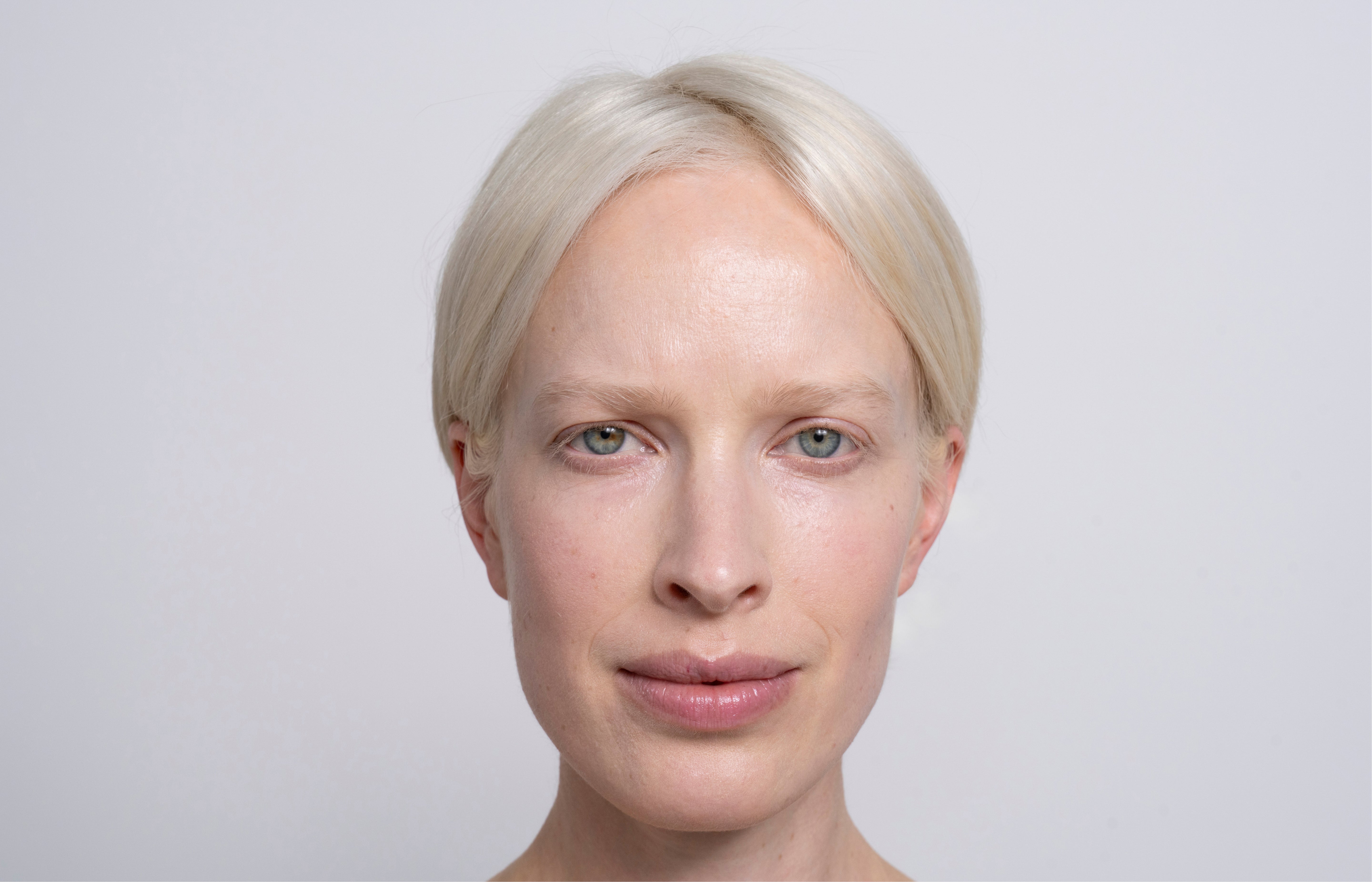 Een vrouw met wit haar en blauwe ogen kijkt vermoeid in de camera.